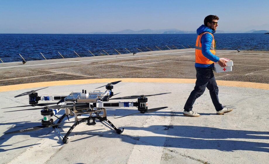 La foto raffigura il drone cargo sanitario su una piattaforma di decollo in riva al mare, mentre un operatore si appresta a caricare il materiale sanitario sul drone