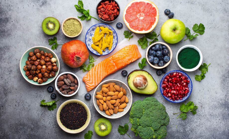 Foto che raffigura molti alimenti sani disposti su un piano, tra cui salmone, frutta secca, mela, arance, ecc per evocare il concetto di alimentazione e prevenzione oncologica