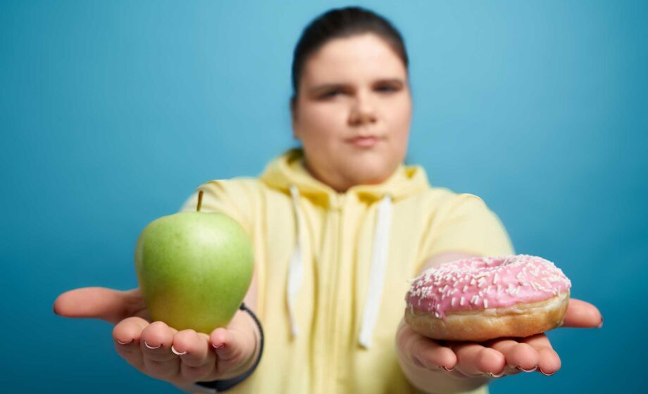 Adolescente obeso che tiene in mano una mela e una ciambella dolce