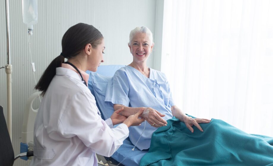 Infermiere in attività di cure palliative che tiene la mano ad un paziente steso su un letto